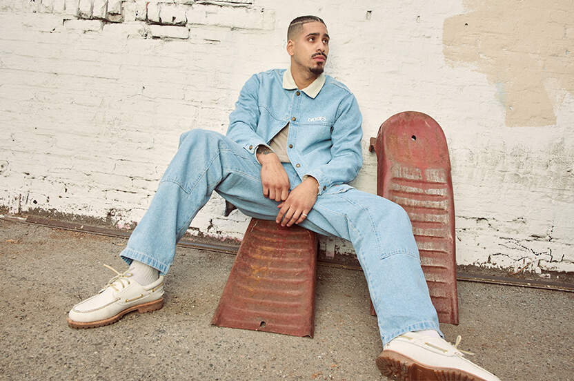Man wearing Dickies Herndon jacket and jeans sitting in front of a brick wall