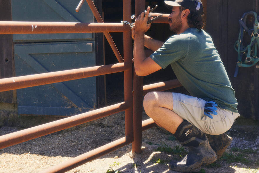 man crouched down fixing a metal fence