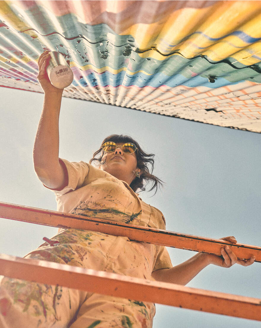 Women spray painting mural in paint splattered jumpsuit