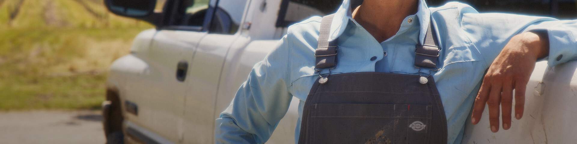 Woman in overalls leaning up agains a pickup truck