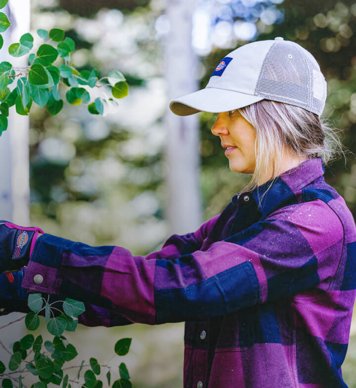 A woman wearing a flannel shirt pruning a bush.