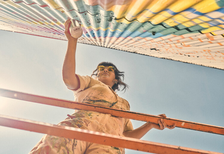 A woman spray-painting a corrugated fence.