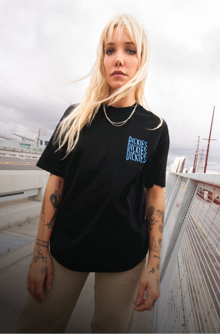 A woman sitting on a ledge wearing the latest styles from Dickies.
