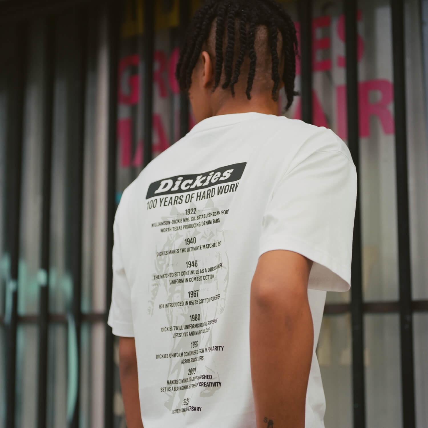 A man sitting on a bench wearing a one hundred years dickies graphic tee shirt