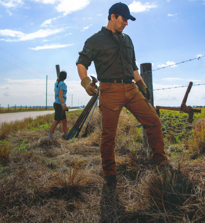 A man looking down at barbed wire fence while holding pliers.