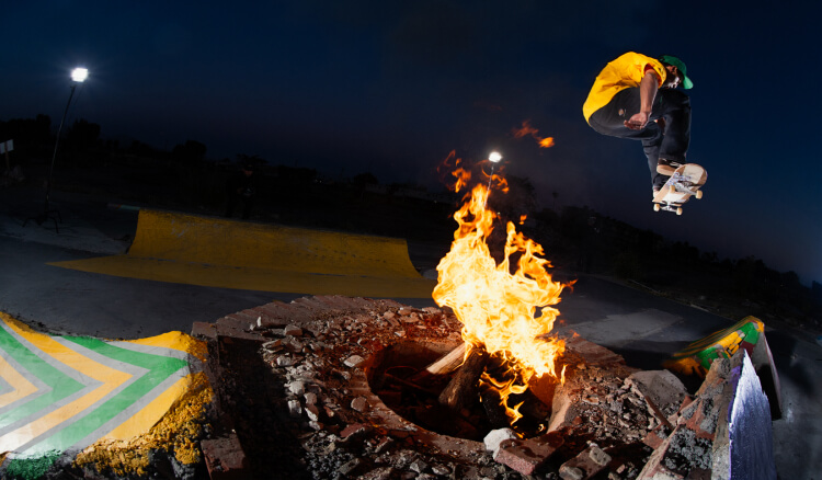 A skater jumping off a ramp over a fire pit at night