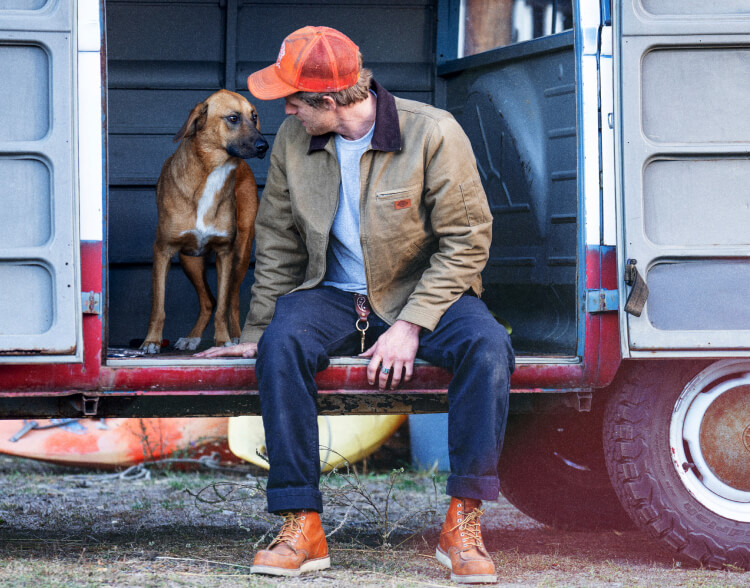 A man sitting on a trailer looking at a dog.