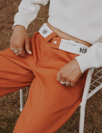 A person wearing a pair of orange out-tucked 874 pants.
