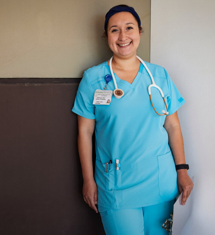 A nurse smiling while standing in front of a wall.