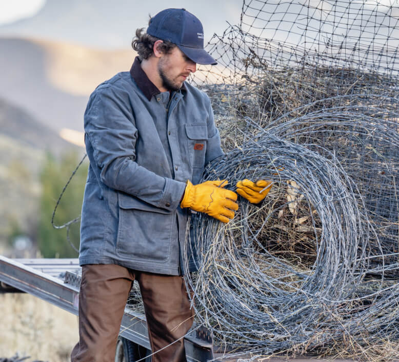 A worker holding rolled up barbed wire fence outside.
