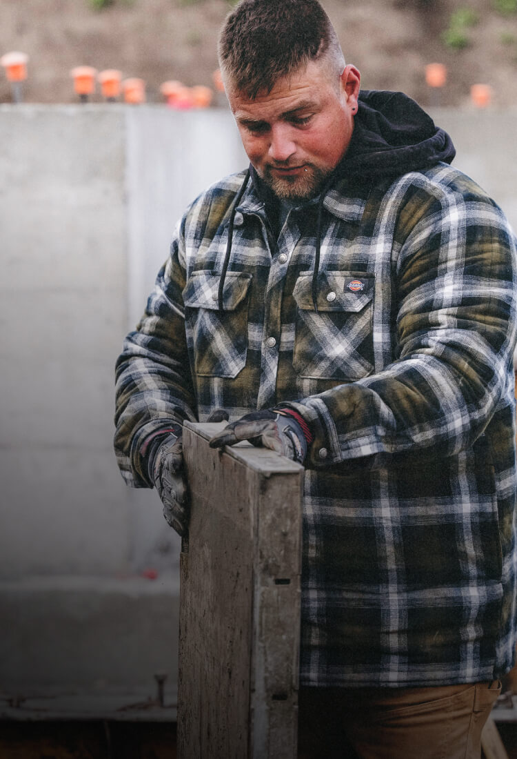 A man looking at a piece of wood wearing a shirt jacket.