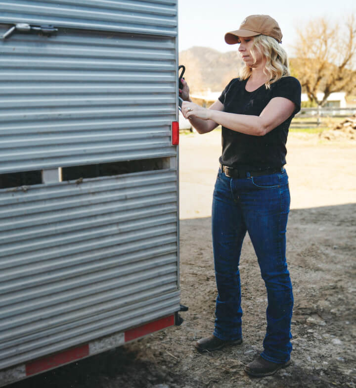 A woman outside locking a trailer wearing a black shirt and perfect shape pants.