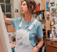 a woman painting while wearing white bib overalls