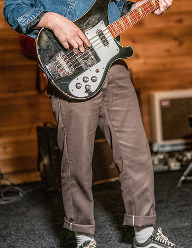 lower half of a person playing a worn bass guitar in a studio