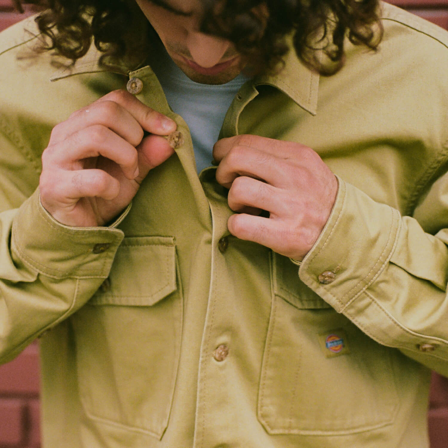 A man buttoning up his full sleeve collared twill shirt