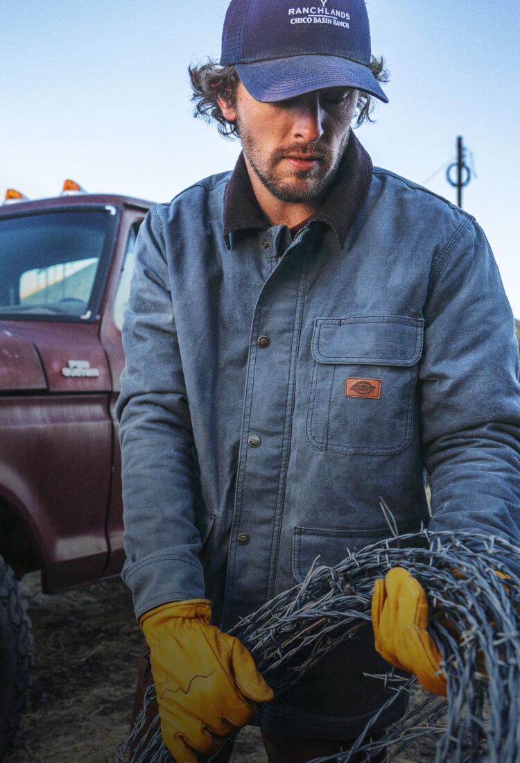 A worker wearing a denim style wax jacket working outside.