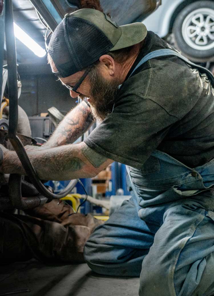 A man wearing denim overalls working on a car.
