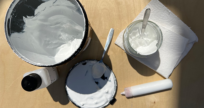Top down view of white paste and paint supplies on a wood surface.