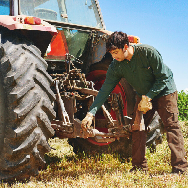 A farm worker setting up a tool on the back of a tractor.