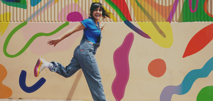 A woman in hickory striped bib overalls jumping and smiling.