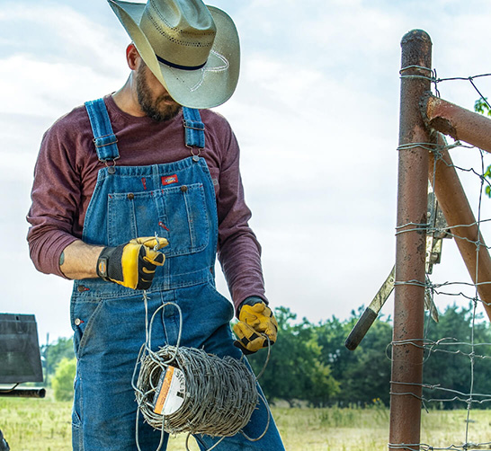 person wearing overalls and gloves with a spool of barbed wire in their hands