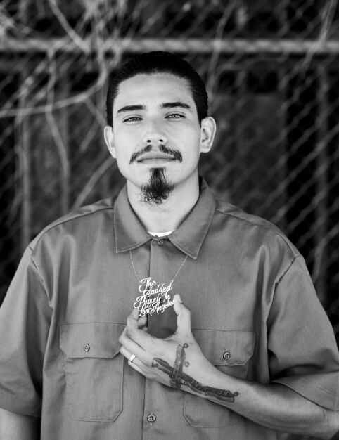 A man in a collared shirt holding a necklace saying 'The Saddest Puppet in Los Angeles'.