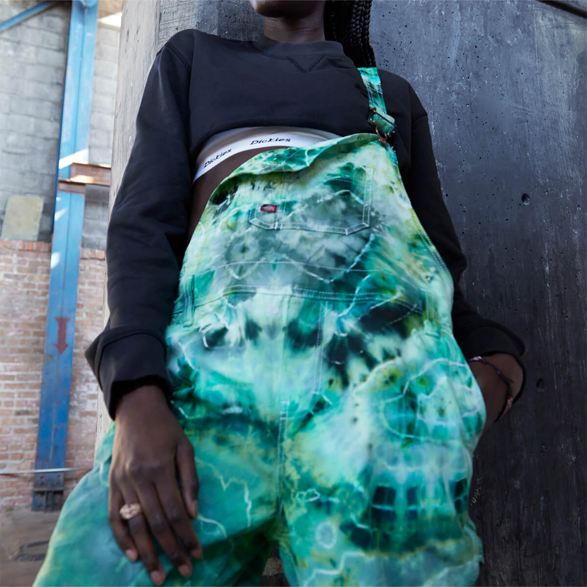 A bib overall altered with colored in a green and teal tie-dye color worn on a model.